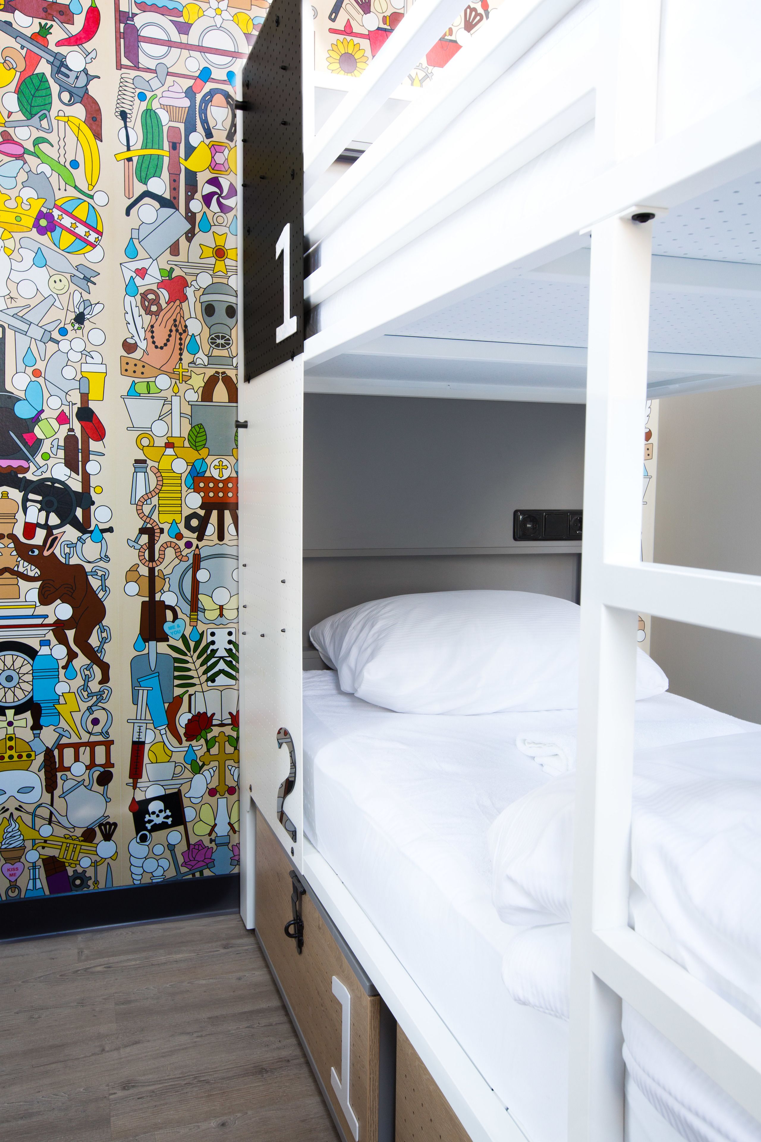 Une chambre avec un lit superposé, un mur décoré d’une fresque colorée, un lit blanc et un plancher en bois.