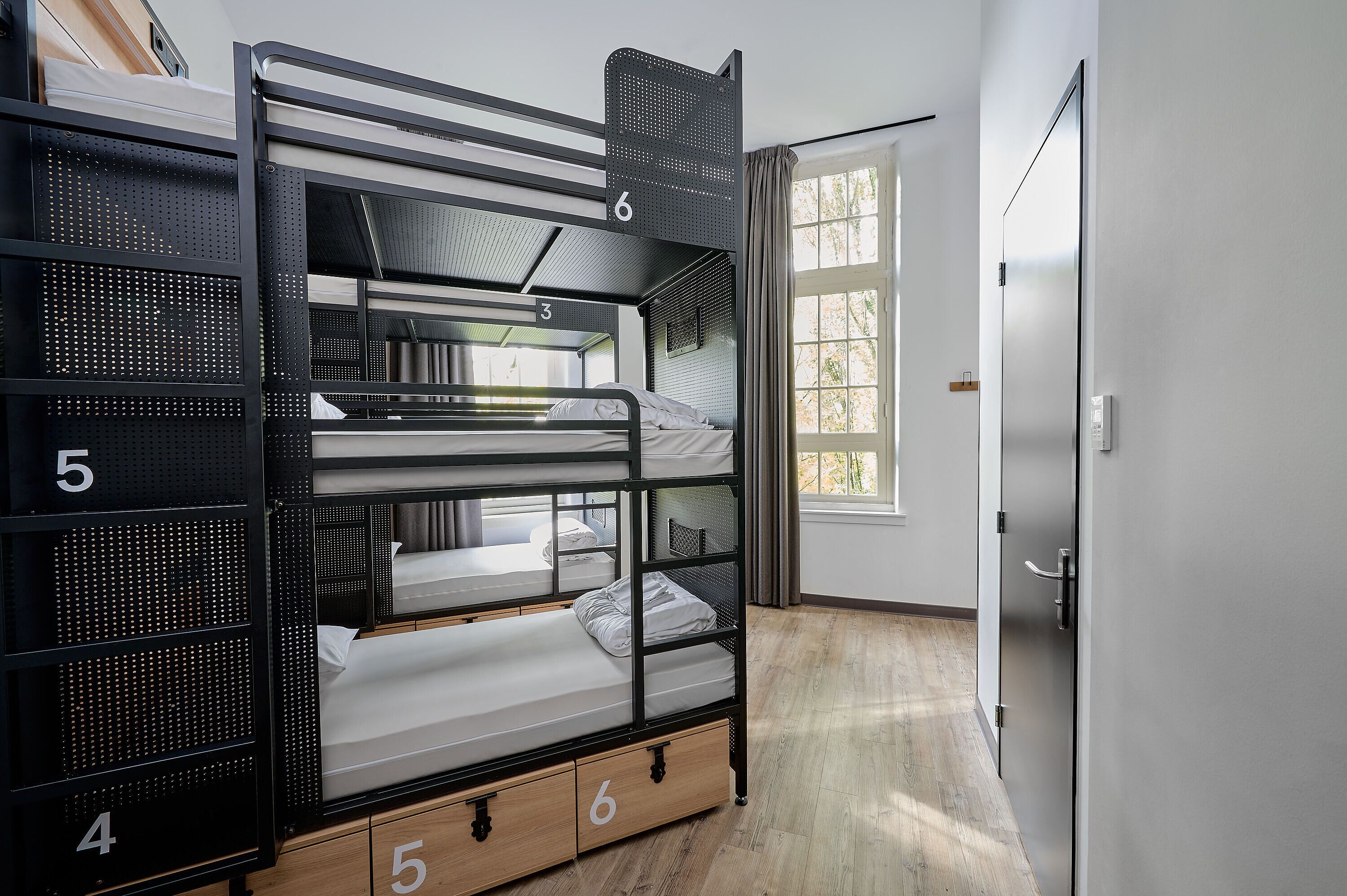 A bunk bed room with three levels, numbered 3, 4, 5, and 6, and a wooden floor.