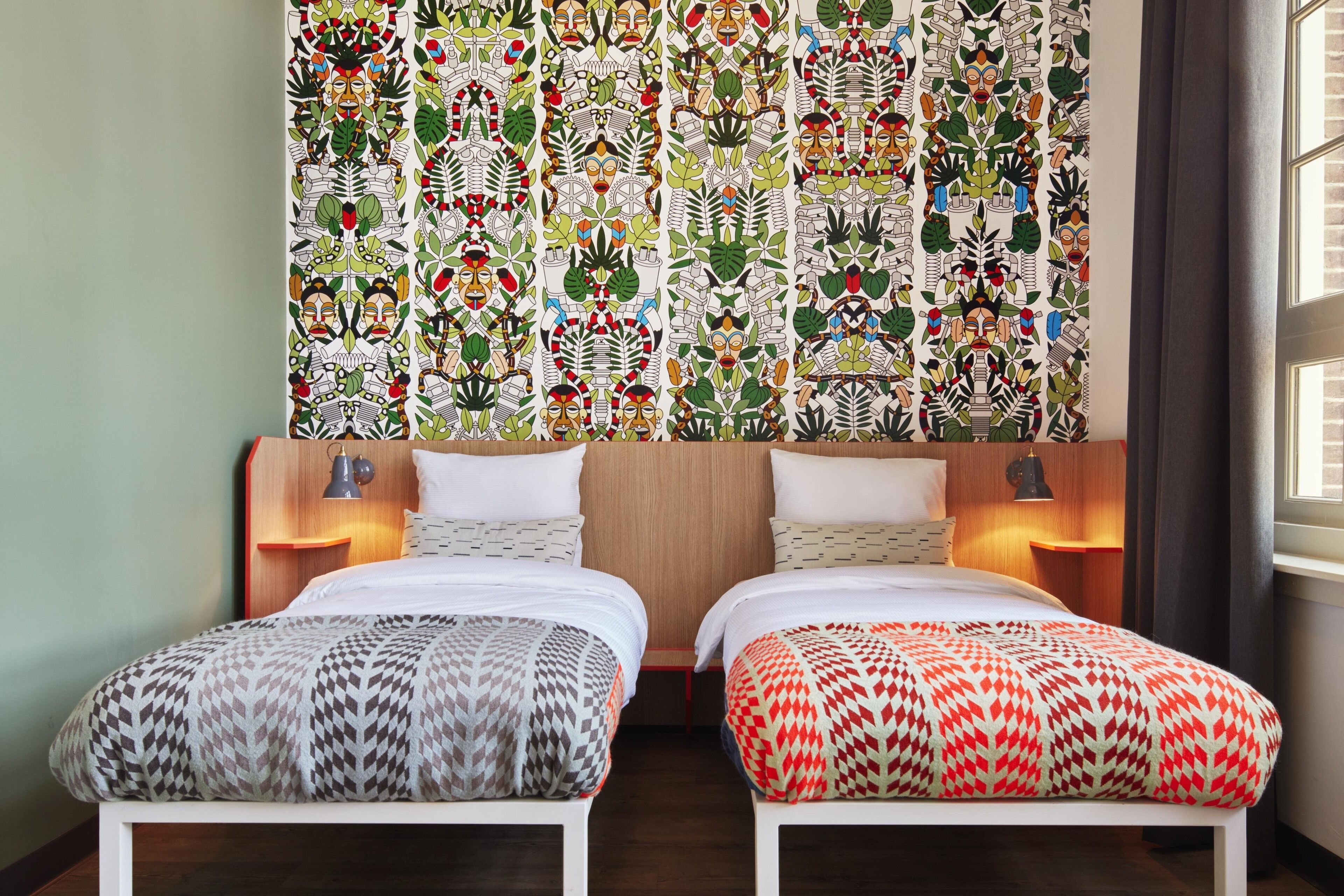 A hotel room with two beds, a wooden headboard, bedside lamps, and a patterned wall mural.