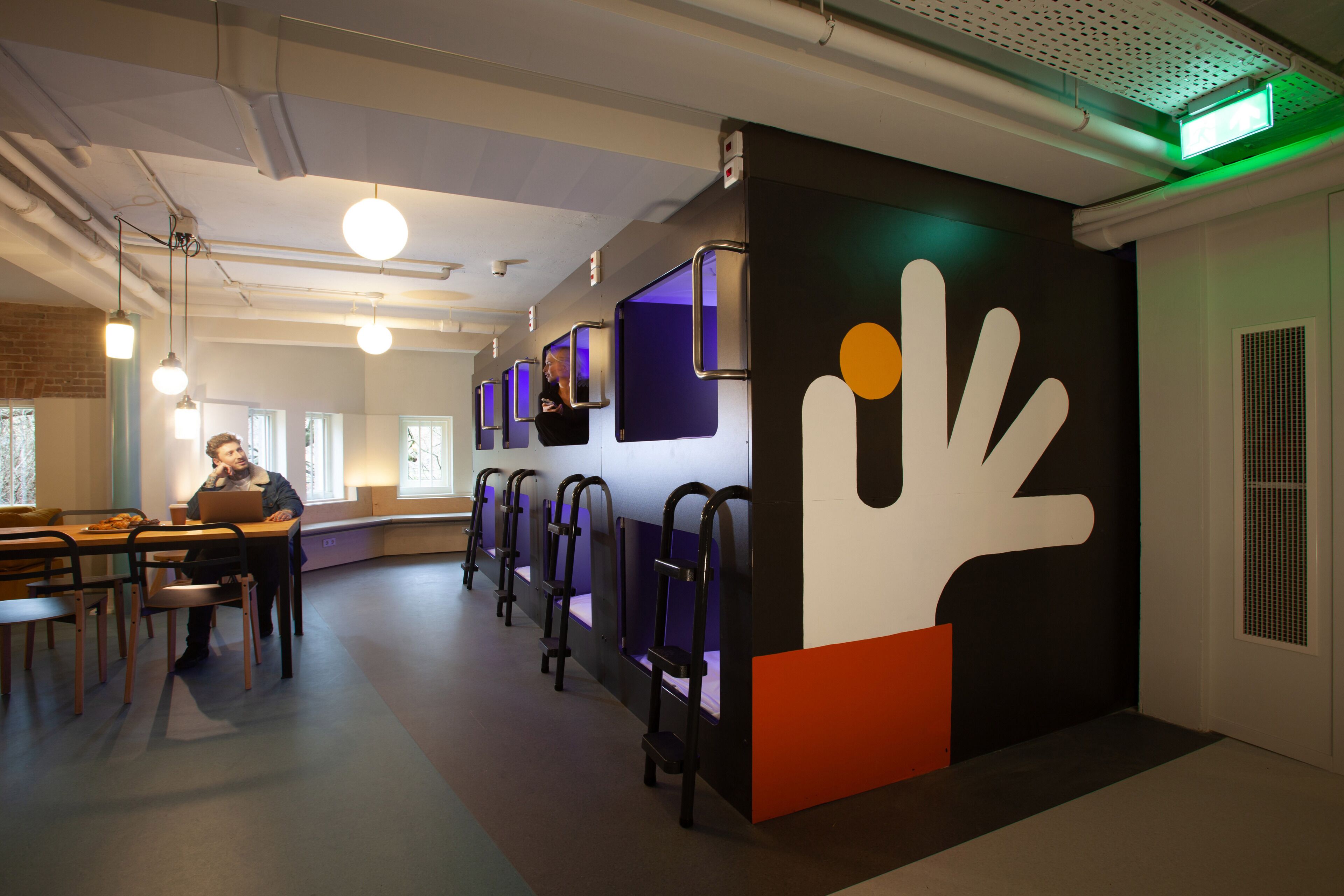 A modern interior with seating areas, a large wall art piece, and a person working at a desk.