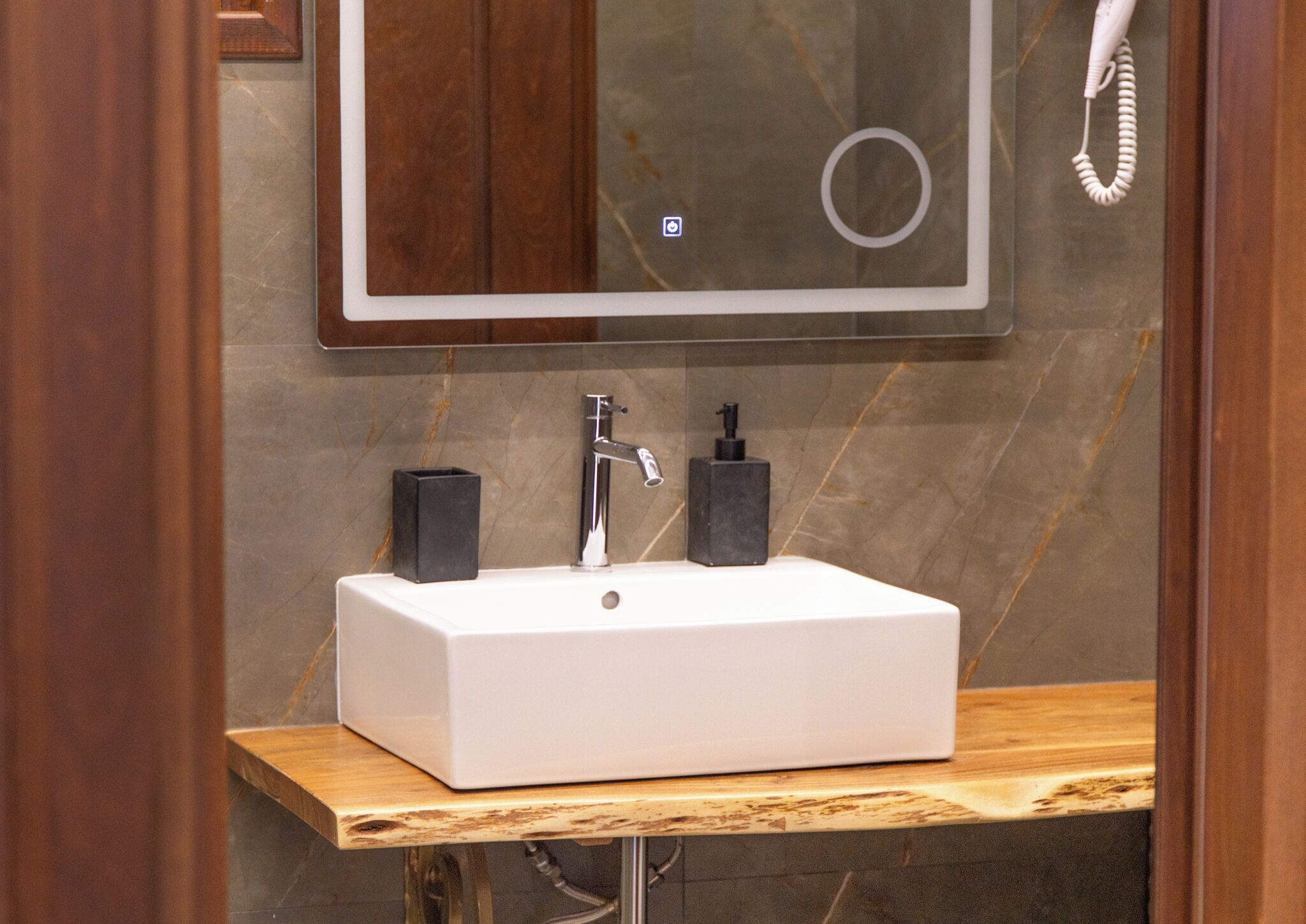 A bathroom with a white rectangular sink, a mirror, a telephone, and a black soap dispenser.