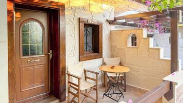 Una puerta de madera con un panel de vidrio, una mesita con sillas y una pared de piedra con una ventana que dice 'Étnico'.