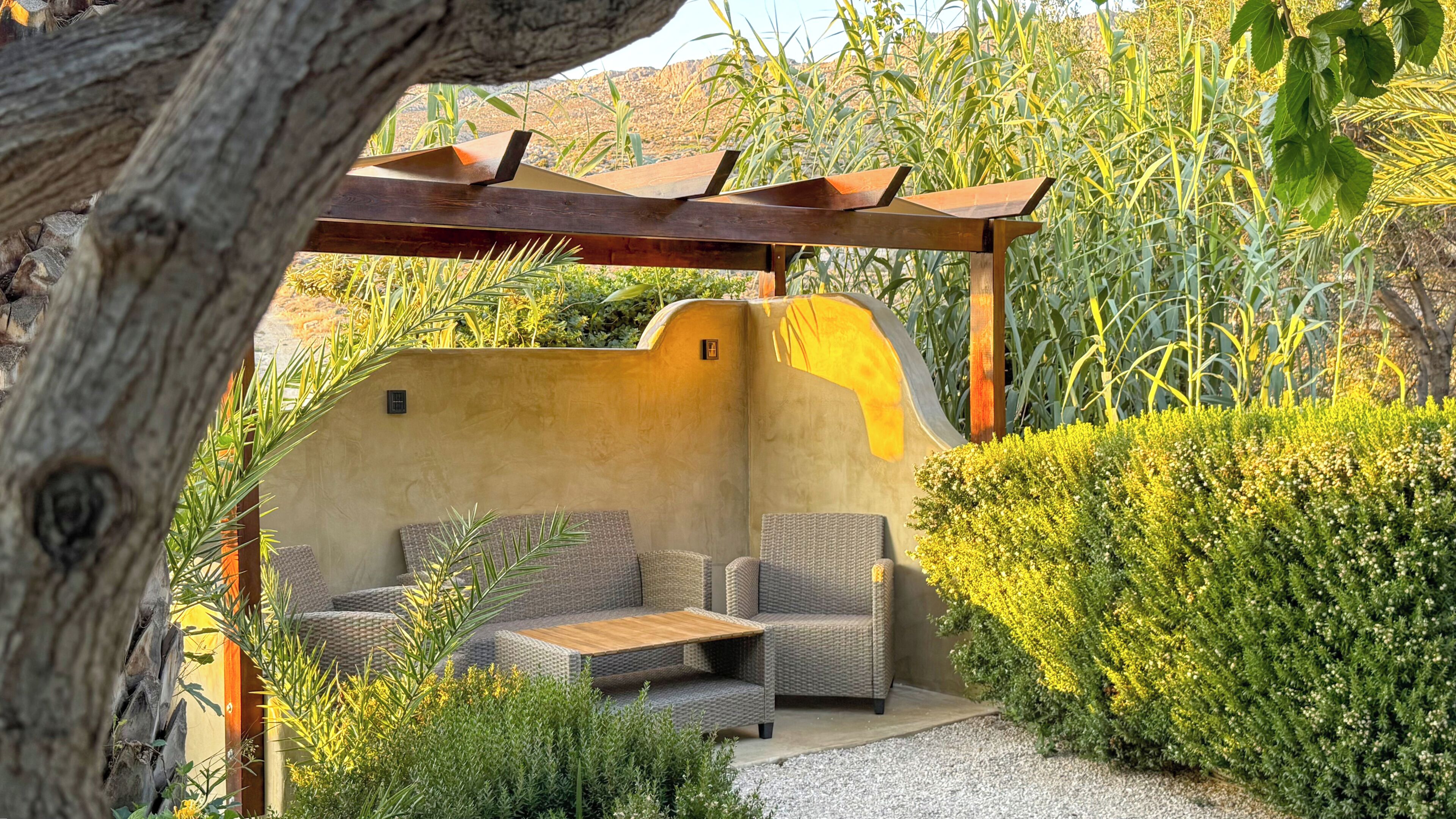 An outdoor patio with wicker furniture, a pergola, and a wall with a small window.