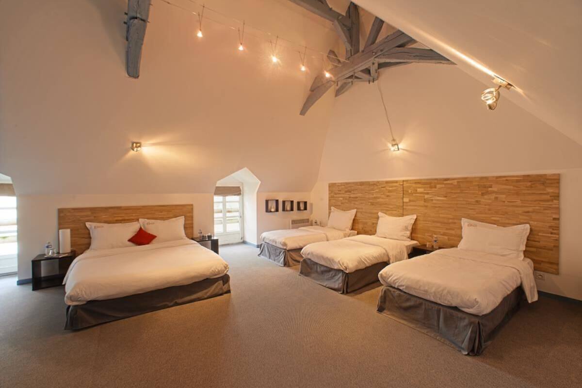 A spacious bedroom with three beds arranged in a row, wooden headboards, and a sloped ceiling with exposed beams.