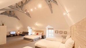 Un amplio dormitorio en el ático con tres camas, un televisor y una zona de estar acogedora.