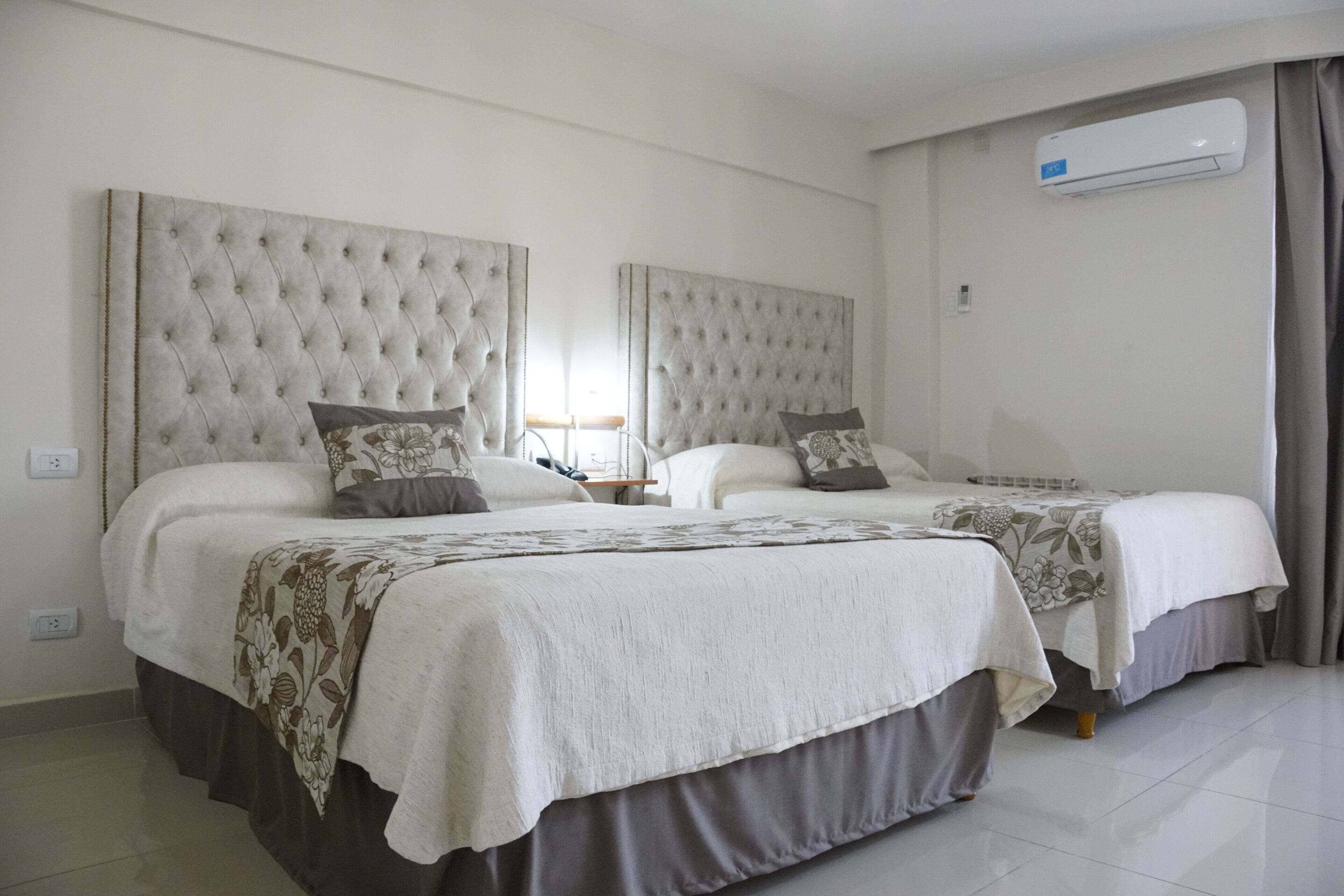 Une chambre d’hôtel avec deux lits, chacun doté d’une tête de lit capitonnée, d’une table de chevet et d’une lampe. Un climatiseur est fixé au mur.