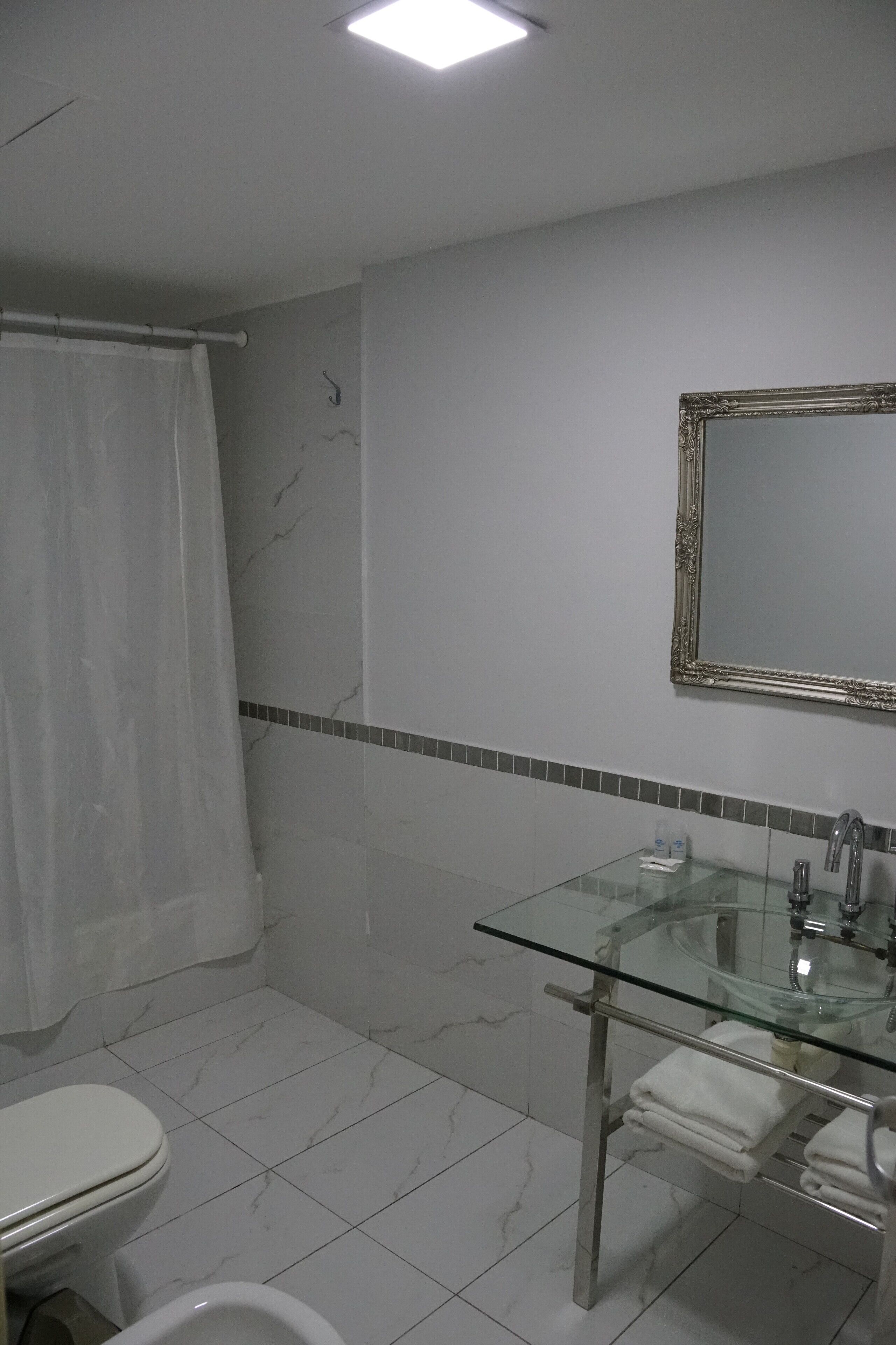 A bathroom with a glass sink, a toilet, a shower curtain, and a mirror.