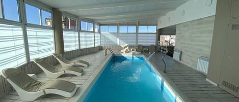 An indoor swimming pool with lounge chairs and a view of the city.