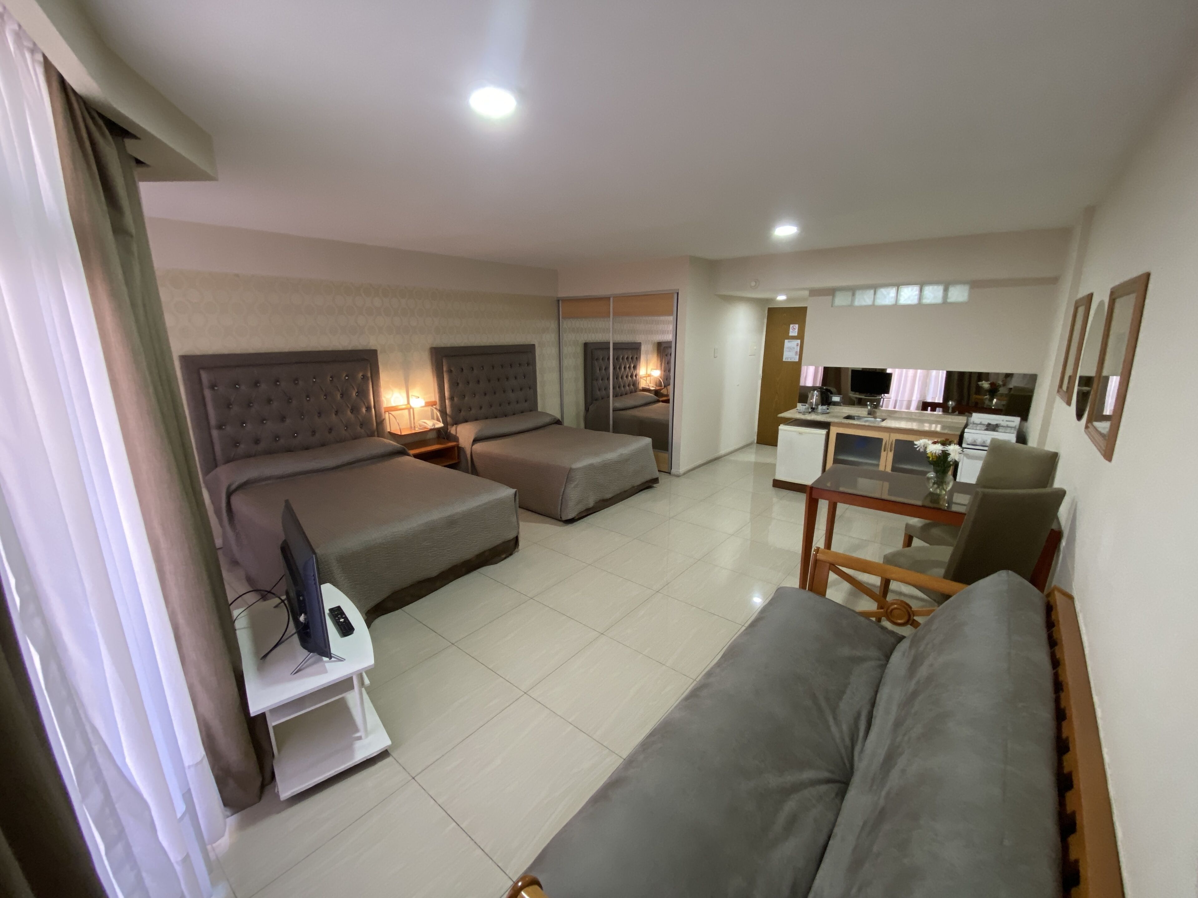 Une chambre d’hôtel avec deux lits, un canapé, une petite kitchenette et une télévision.