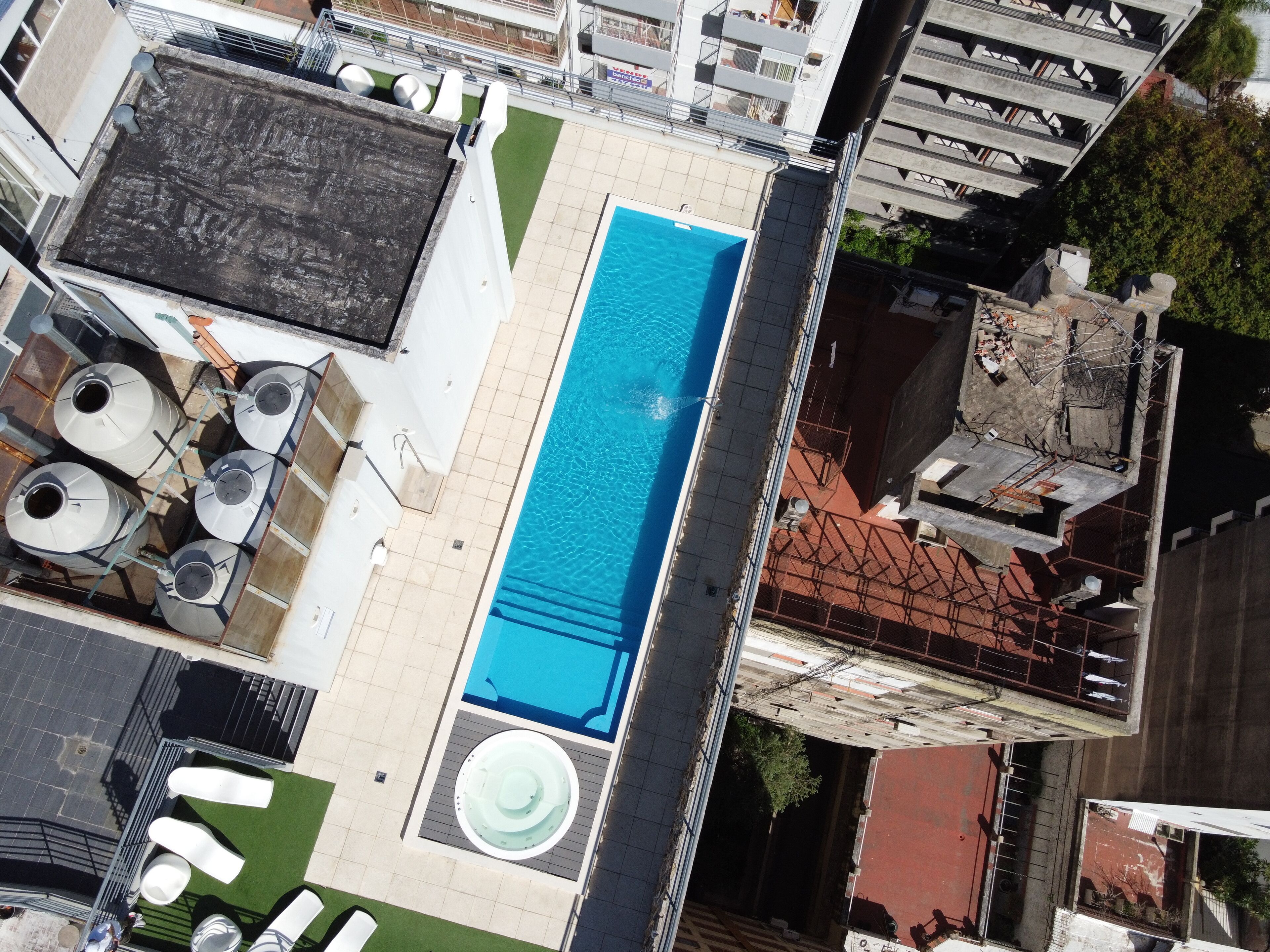Una piscina en la azotea con un jacuzzi, rodeada de mobiliario exterior y vistas a la ciudad.