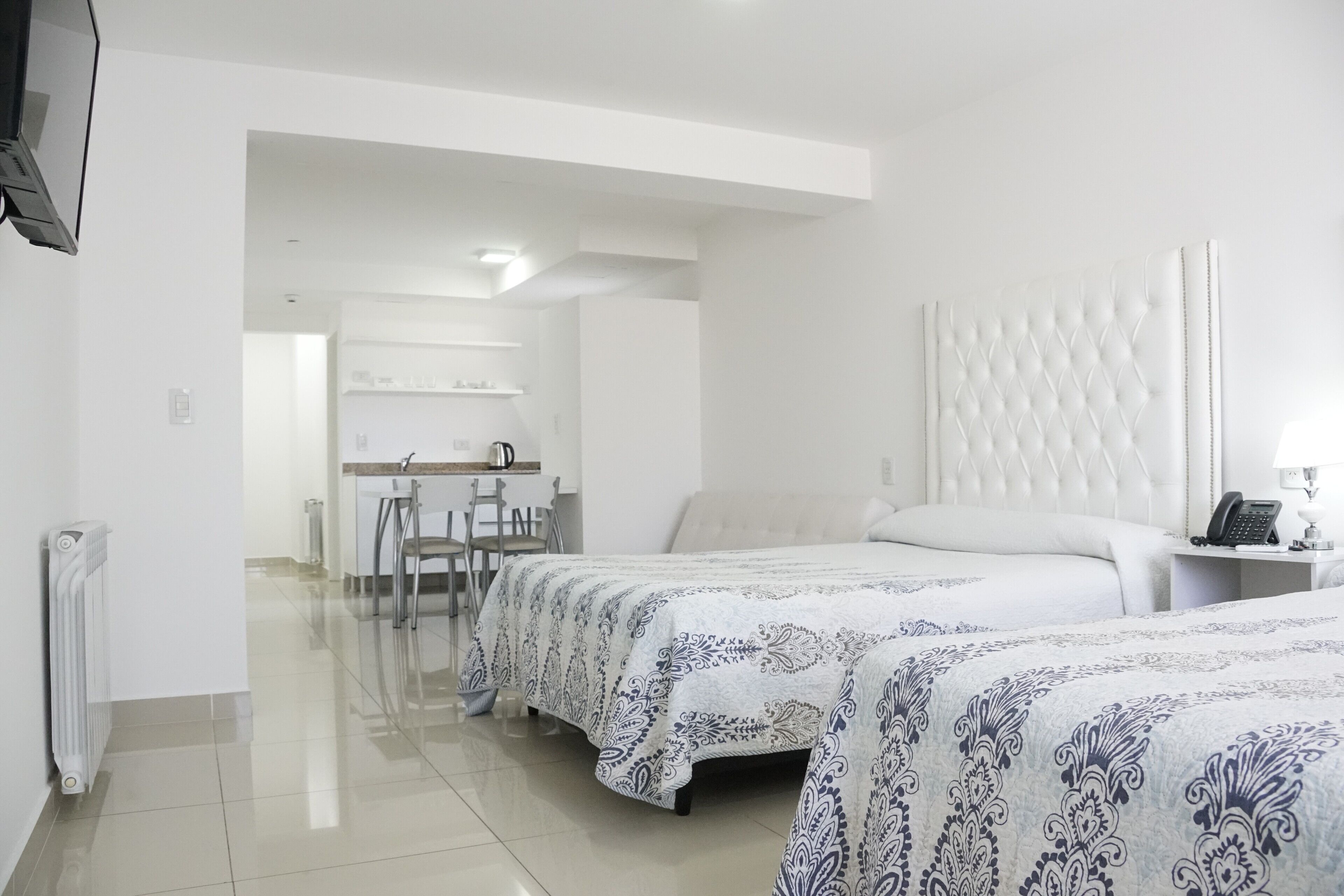 A hotel room with two beds, a sitting area with a chair and table, and a kitchenette in the background.