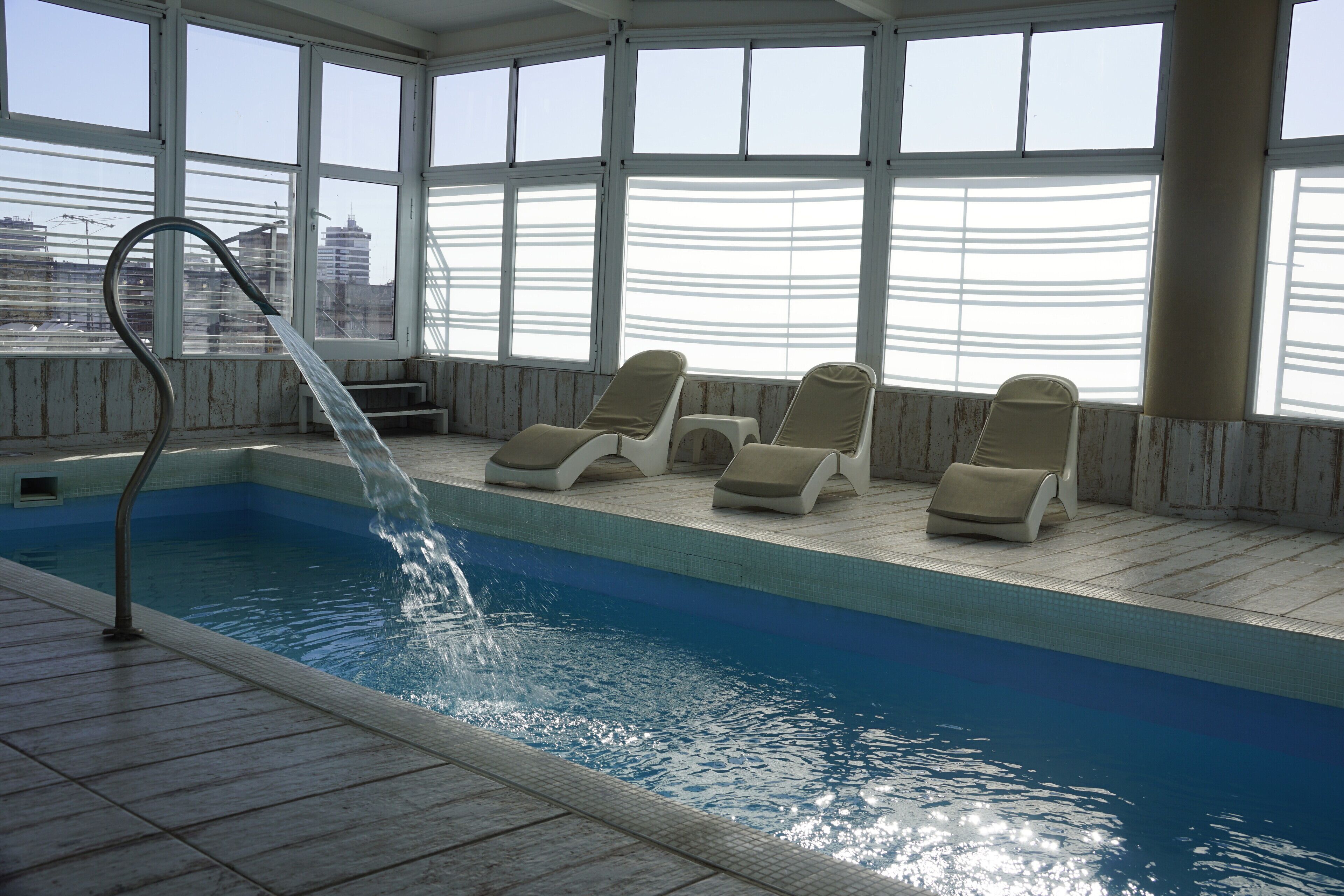 An indoor swimming pool with clear blue water, a water feature, and lounge chairs along the poolside.