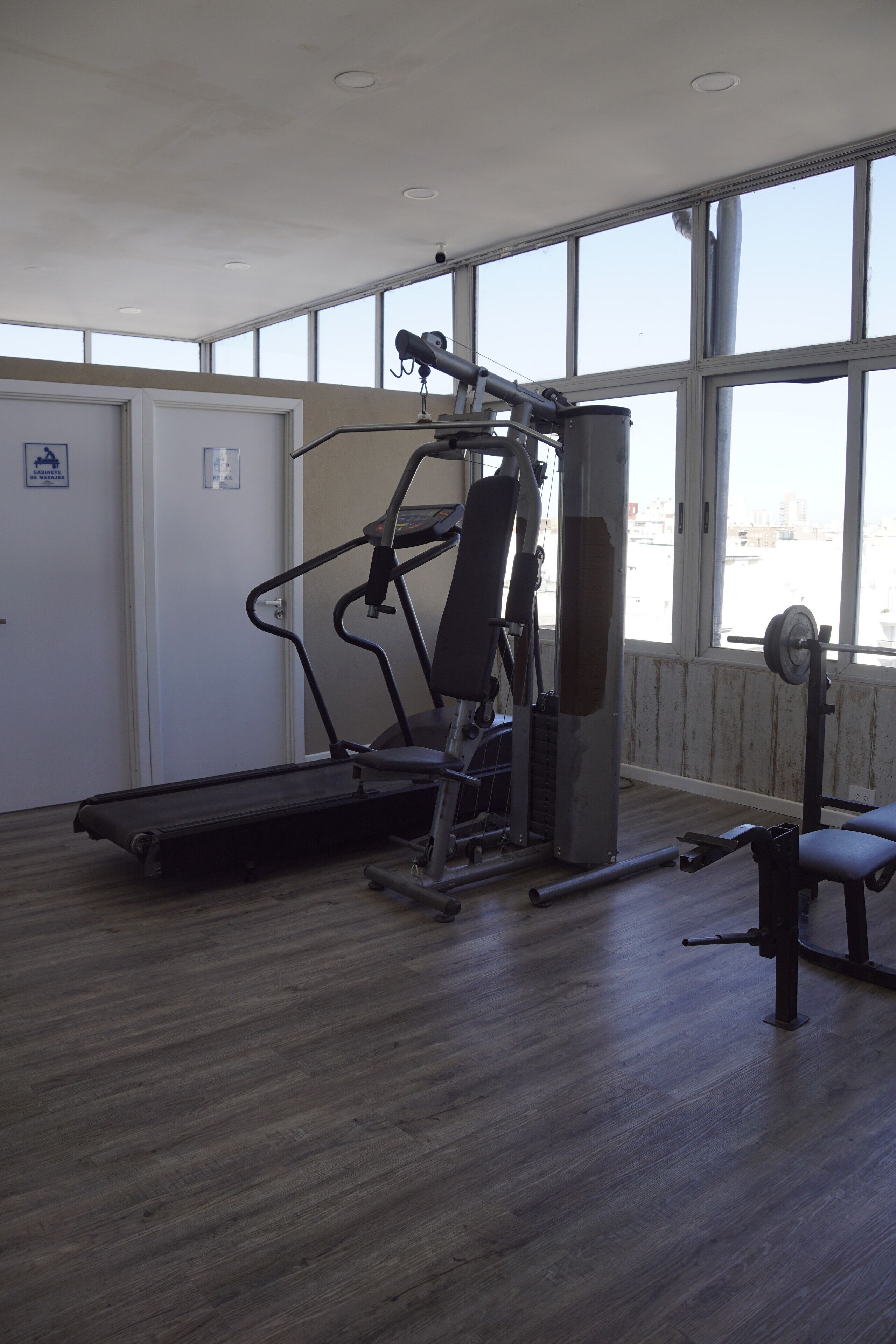 A gym with exercise equipment, large windows, and a wooden floor.