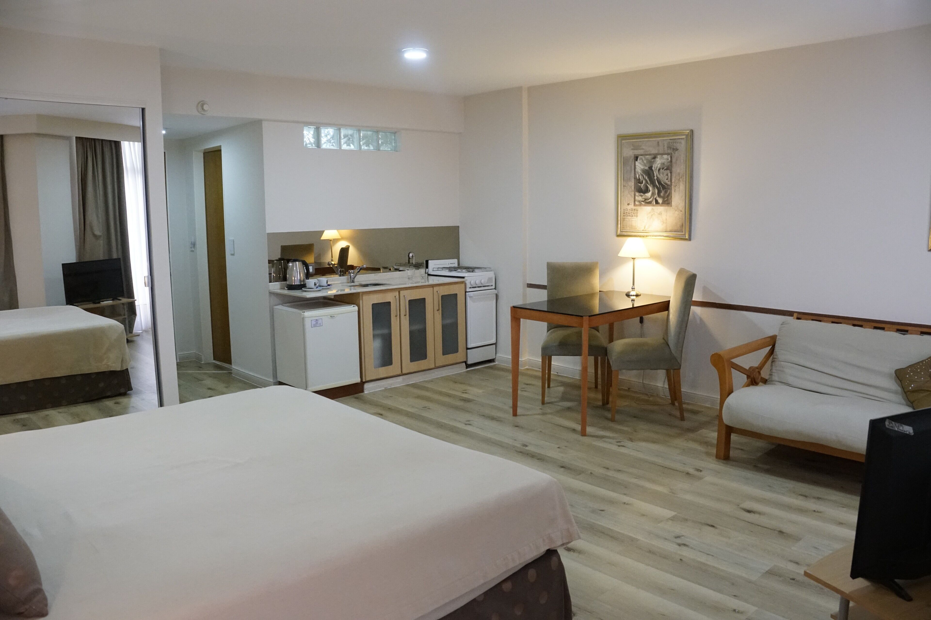 Una camera d'albergo con un letto, una scrivania con una sedia, un angolo cottura e un televisore.