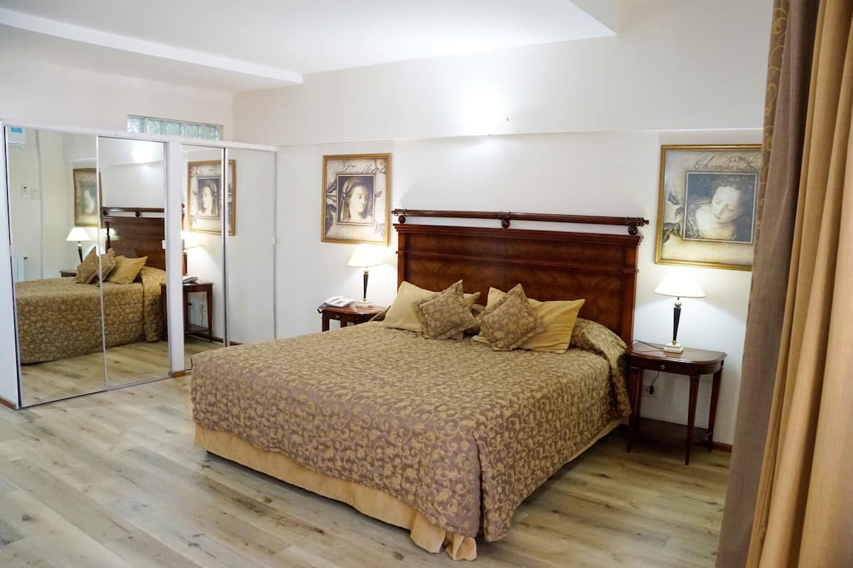 A bedroom with a large bed, a wooden headboard, two bedside tables with lamps, a mirror, and framed artwork on the walls.