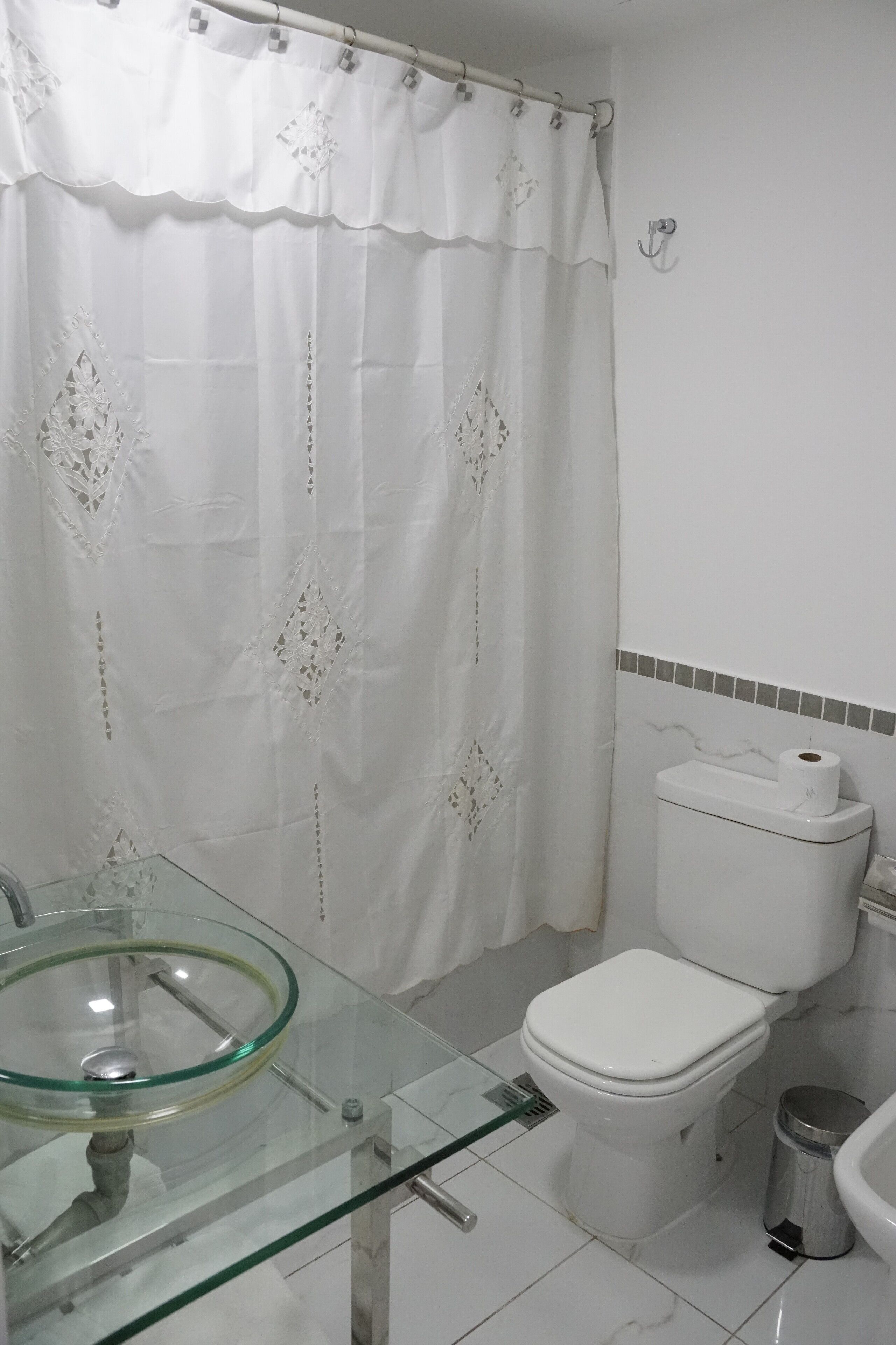 A bathroom with a glass sink, white toilet, and a shower curtain with lace patterns.
