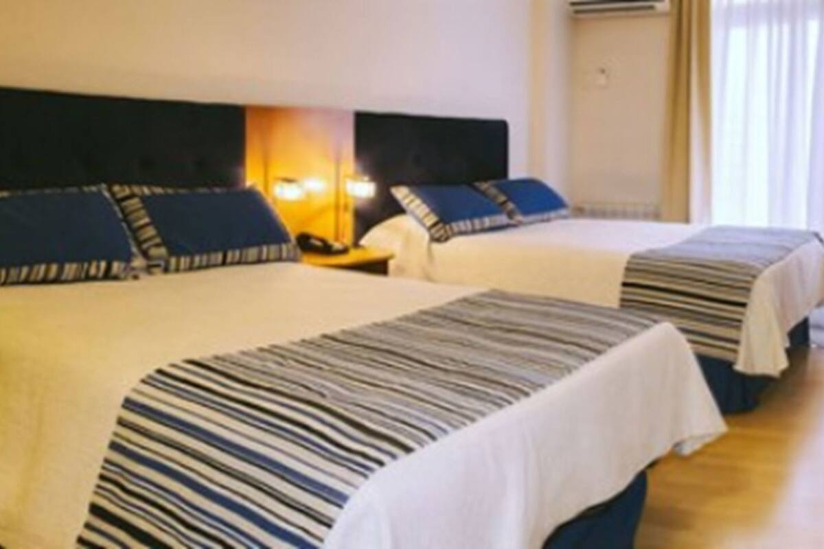 A hotel room with two beds, a desk, a television, and a window with curtains.