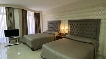 Quarto de hotel com duas camas, uma televisão e uma mesa de cabeceira com abajur.