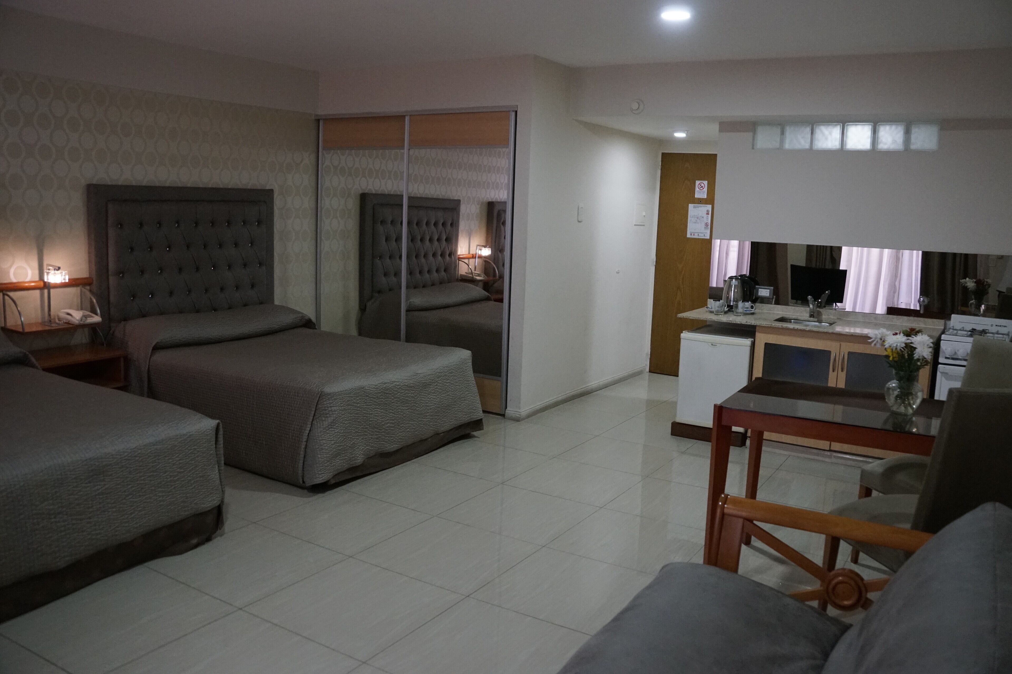 A hotel room with two beds, a desk, a chair, and a small kitchenette.