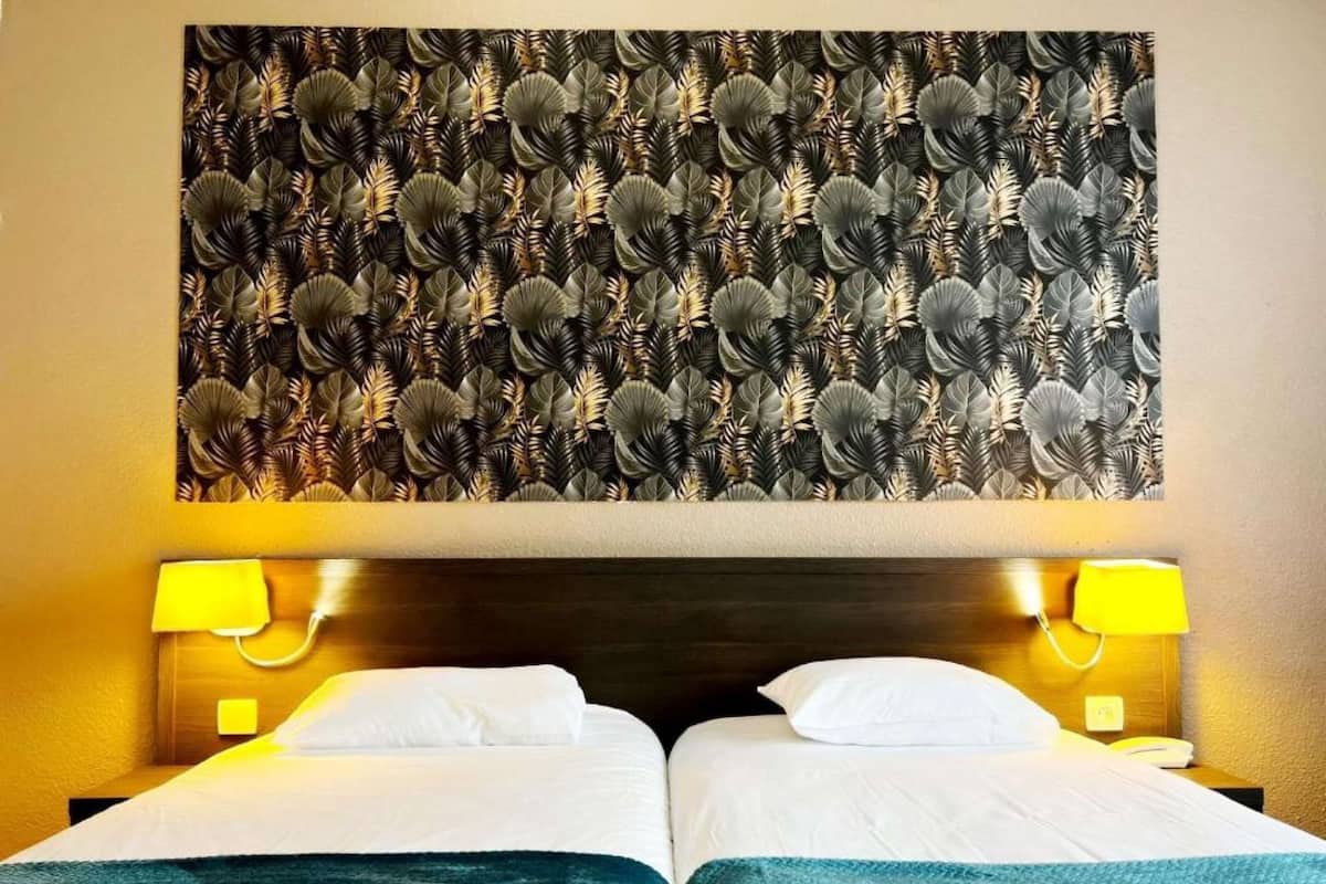 Une chambre d’hôtel avec deux lits, une grande tapisserie murale et deux lampes de chevet.