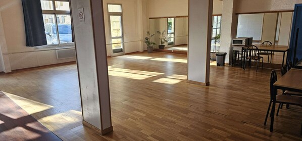 A spacious room with wooden flooring, large windows, a dining area with a table and chairs, and a microwave on a counter.