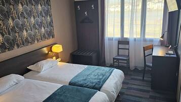 A hotel room with two beds, a desk, a chair, a lamp, and a window with curtains.