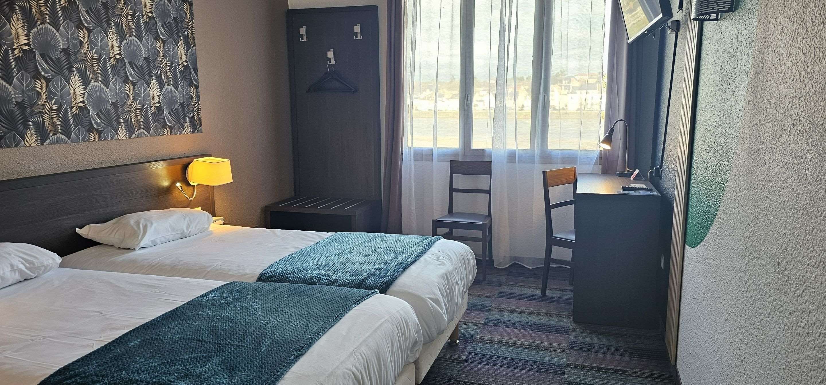 Habitación de hotel con dos camas, un escritorio, una silla, una lámpara y vistas al exterior.