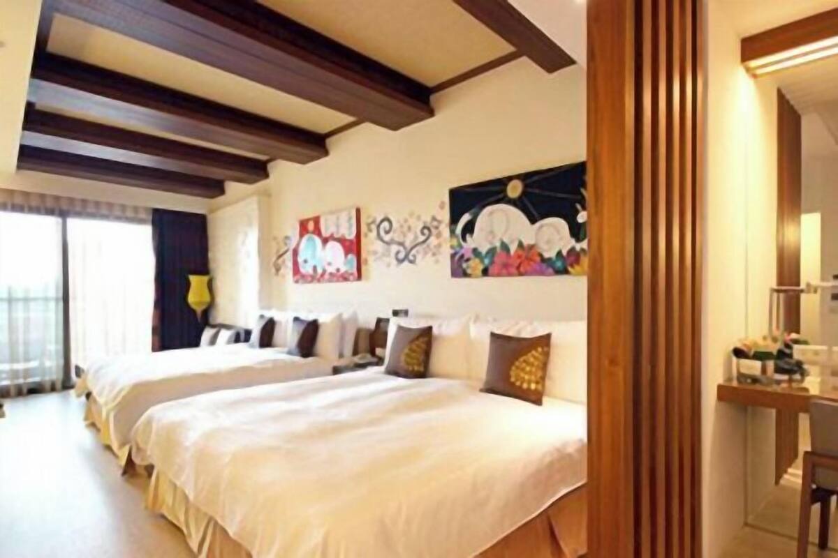 Una habitación de hotel con dos camas, vigas de madera en el techo, obras de arte en las paredes y un escritorio con silla.
