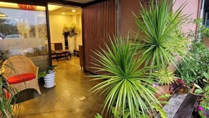 A modern interior with a glass door entrance, a seating area with a wicker chair, and various potted plants. - A&L Inn (Hengchun)