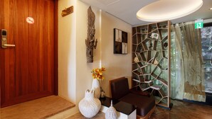 A reception area with a wooden door, a white vase with flowers, a decorative wall piece, a modern chair, and a glass partition with a geometric design. - A&L Inn (Hengchun)