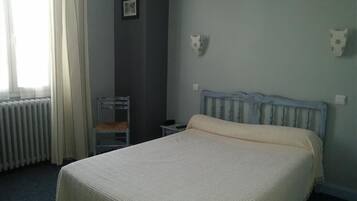 A bedroom with a bed, a chair, a radiator, and a wall-mounted light fixture.