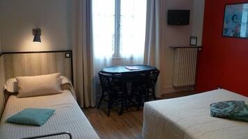 A hotel room with two single beds, a small round table, a TV on the wall, and a window with curtains.