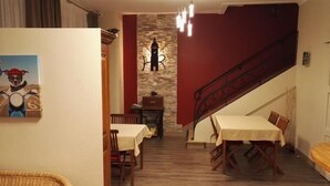 A dining area with two tables, a staircase, and a stone wall with a clock.