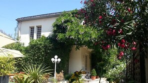 A courtyard with a stone floor, potted plants, a white lamp post, and a building with a tiled roof.