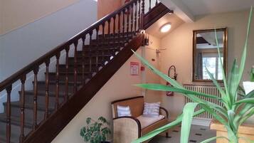 Una escalera con balaustres de madera, un sofá de mimbre con cojines, una planta en maceta y un espejo en la pared.