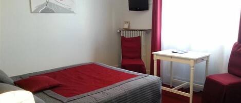 Un dormitorio con una cama, una mesita pequeña, una silla, un radiador y un televisor en la pared.