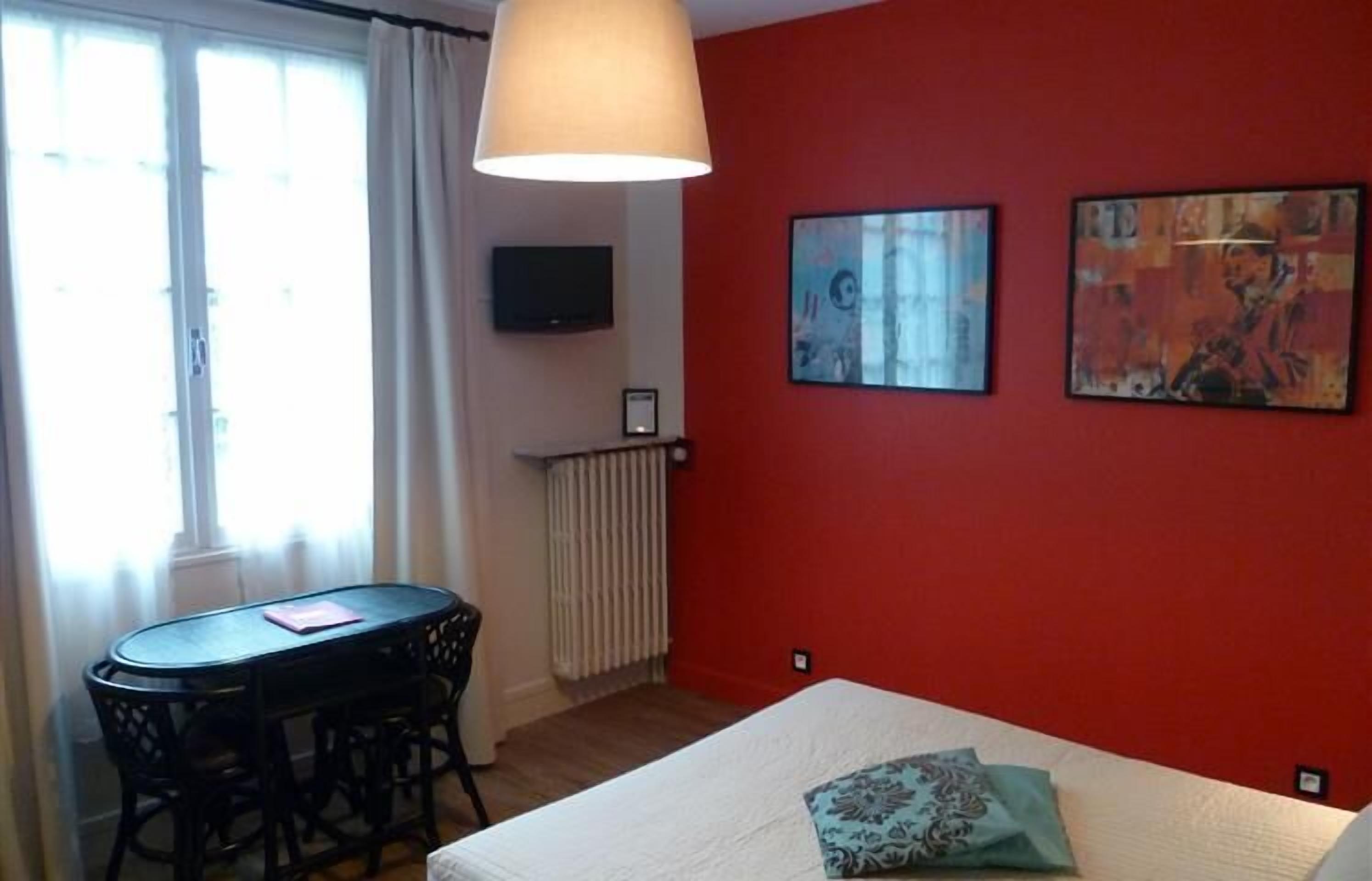 Una habitación con cama, una mesa con sillas, un televisor en la pared y dos cuadros.