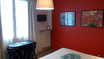 A room with a bed, a table with chairs, a TV on the wall, and two paintings.