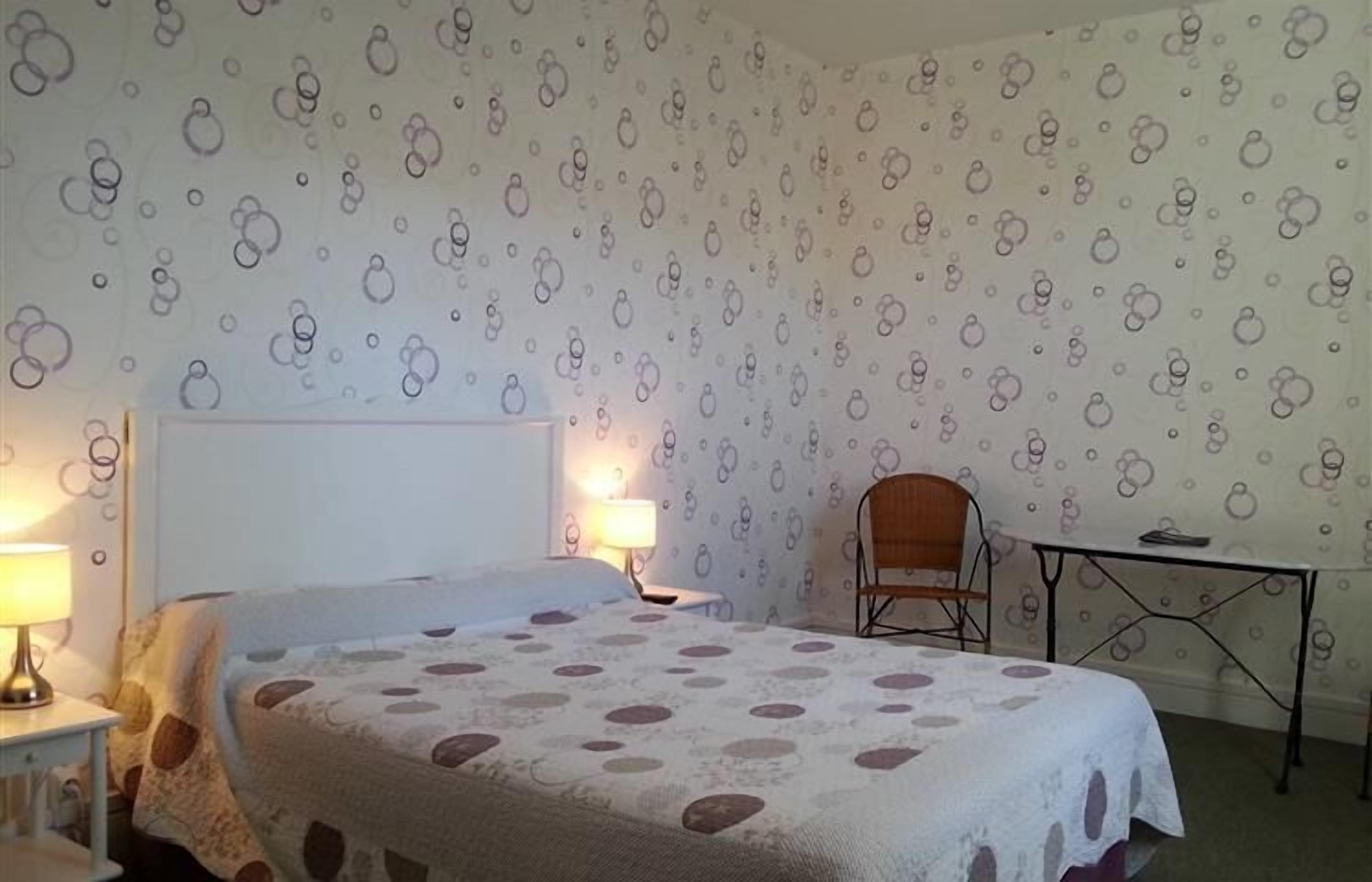 A bedroom with a bed, two bedside lamps, a chair, and a small table.