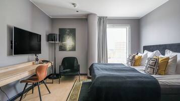 Una habitación de hotel moderna con cama, escritorio, silla, televisor y una obra de arte en la pared.