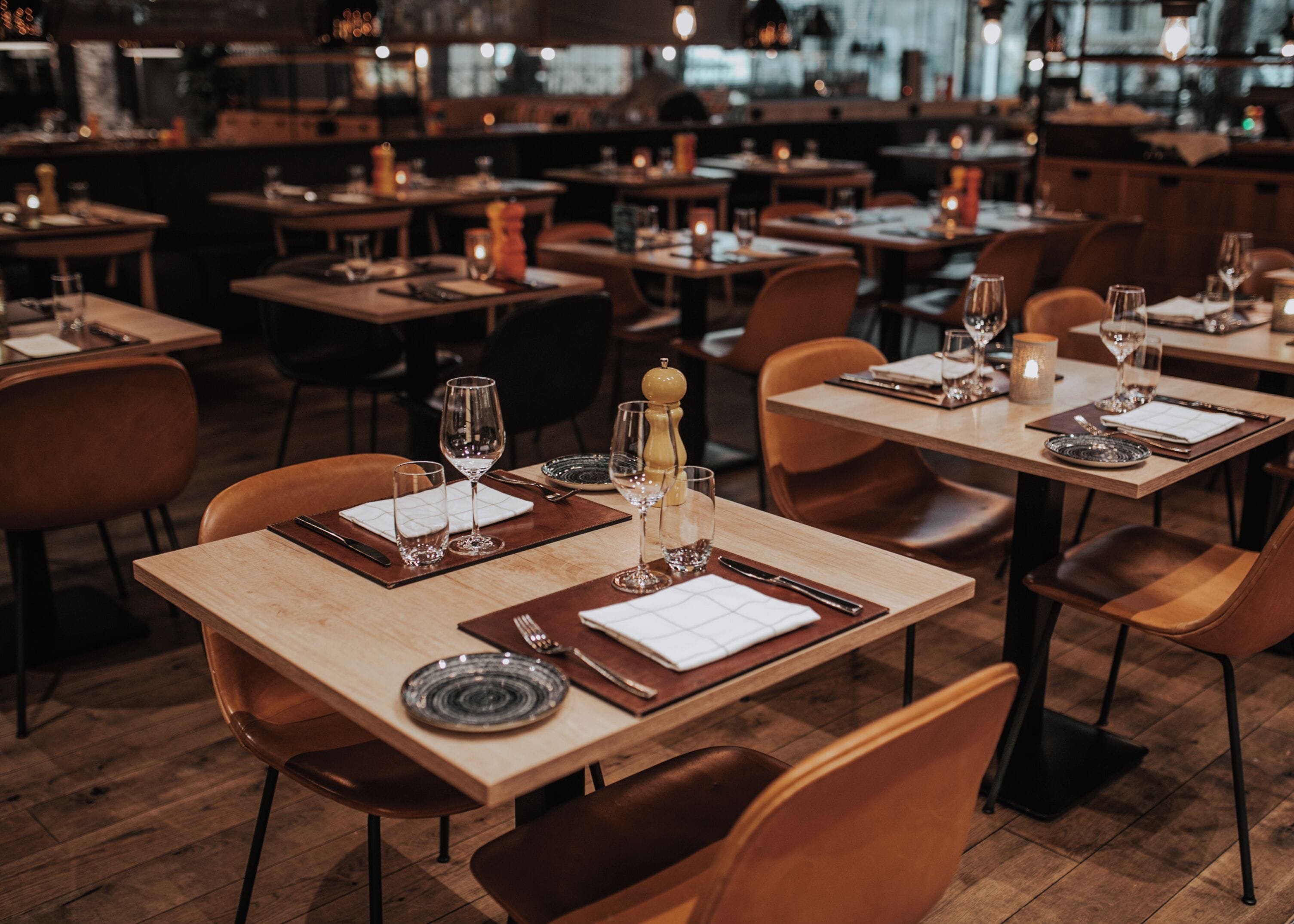 A restaurant interior with multiple dining tables, each set with plates, cutlery, and glasses.