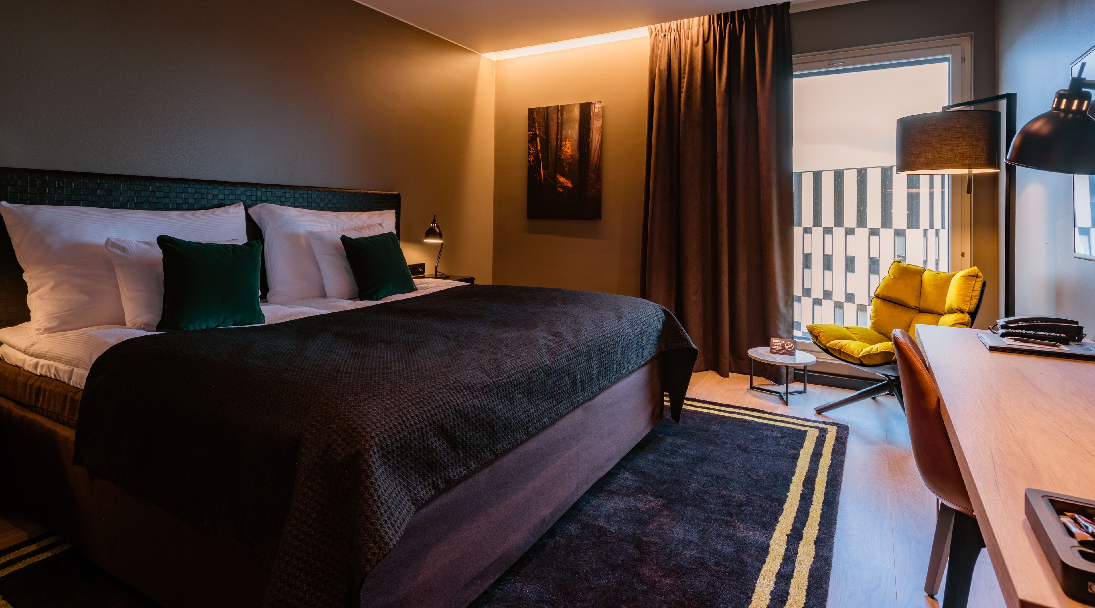 Una habitació d'hotel amb un llit gran, un escriptori, una cadira i vista a la ciutat.
