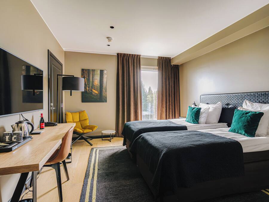 Habitación de hotel con dos camas, un escritorio, una silla, un televisor y una ventana con cortinas.