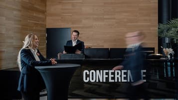Un espace d’accueil avec un mur en bois, un comptoir de réception noir et une enseigne indiquant « CONFÉRENCE ».