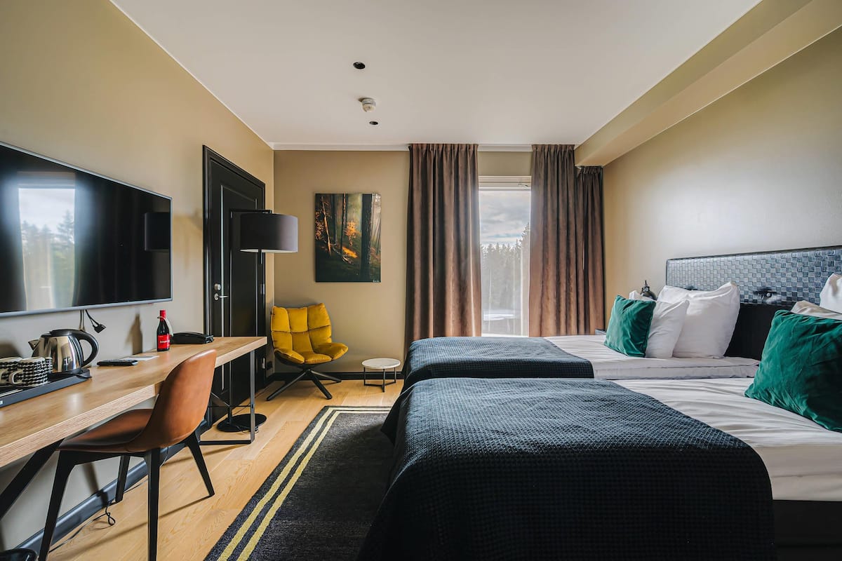Ein Hotelzimmer mit zwei Betten, einem Schreibtisch mit Stuhl, einem Fernseher und einem Gemälde an der Wand.