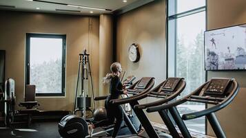 Une salle de sport équipée de tapis de course, d’un banc de musculation et d’une horloge murale.