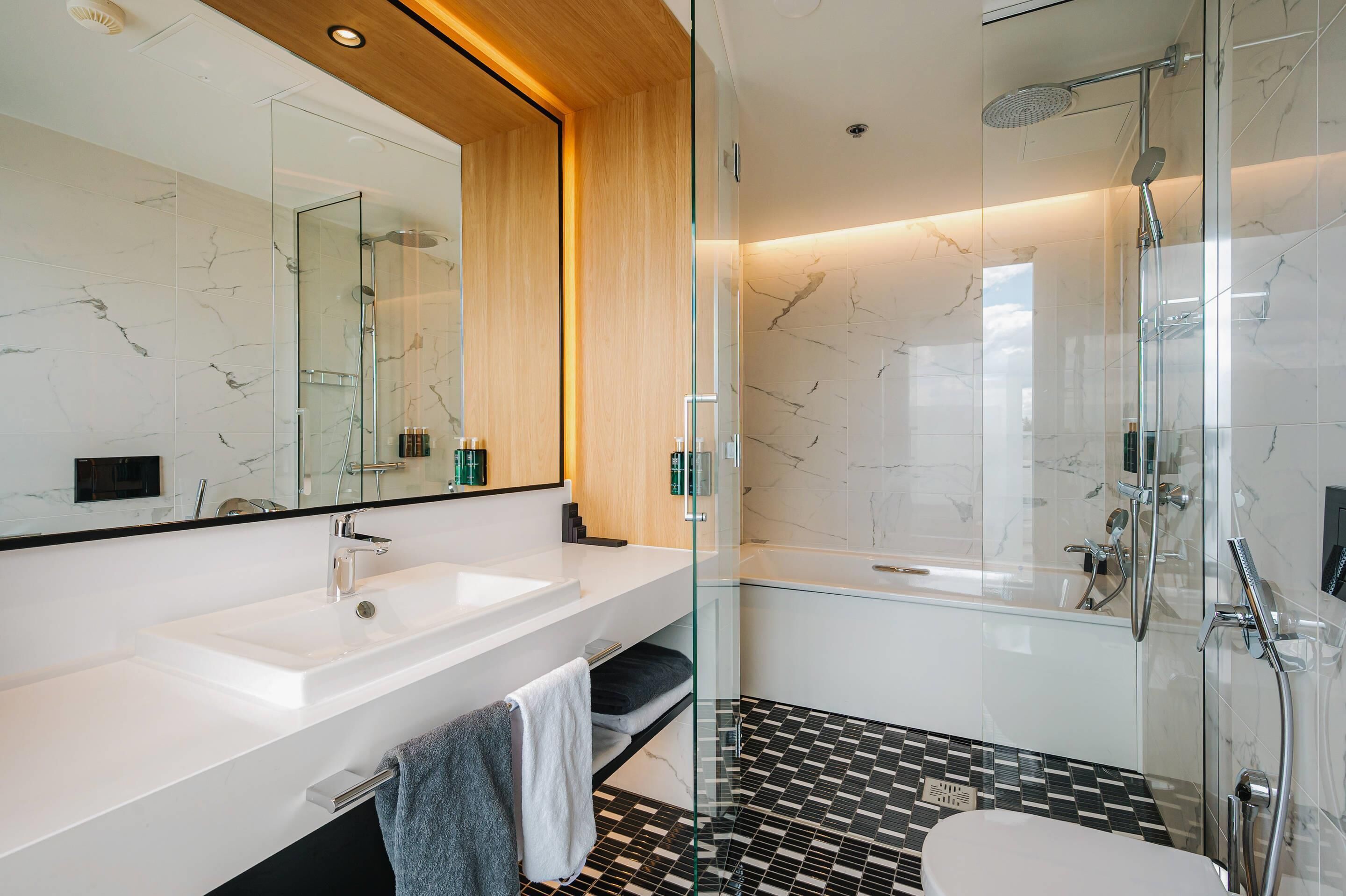 Un bagno moderno con cabina doccia in vetro, lavandino bianco e pavimento piastrellato in bianco e nero.