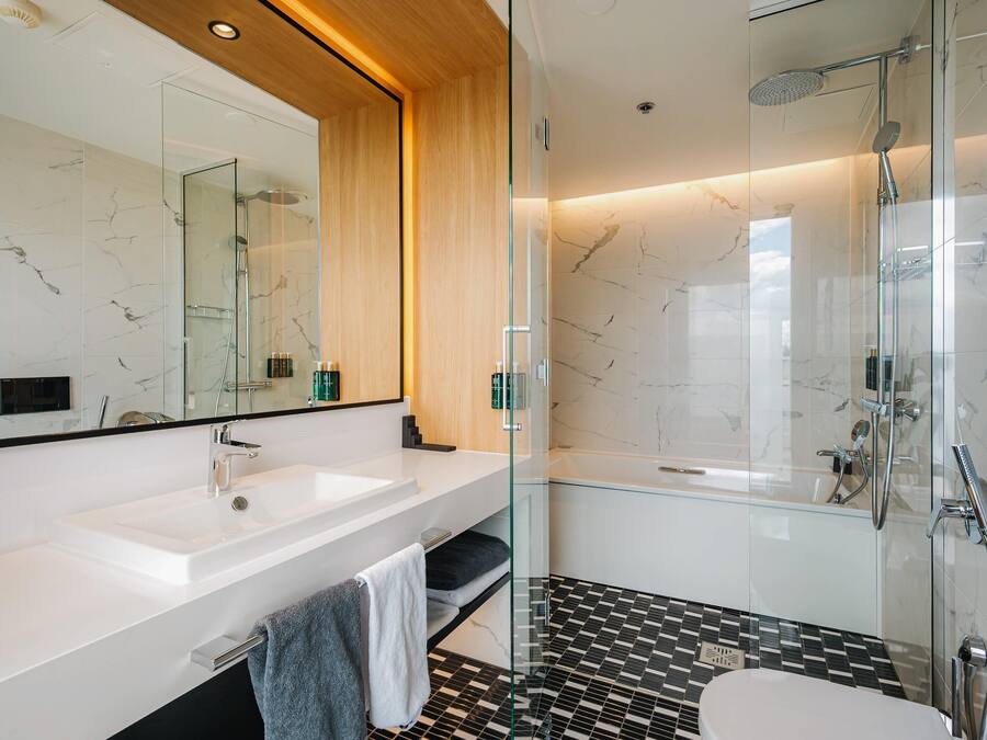 Un bagno moderno con cabina doccia in vetro, lavandino bianco e pavimento piastrellato in bianco e nero.