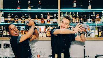 Twee bartenders achter een bar, met rekken vol verschillende drankflessen.