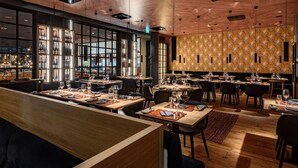 Un restaurante con varias mesas, una zona de bar con botellas y una pared con diseño.